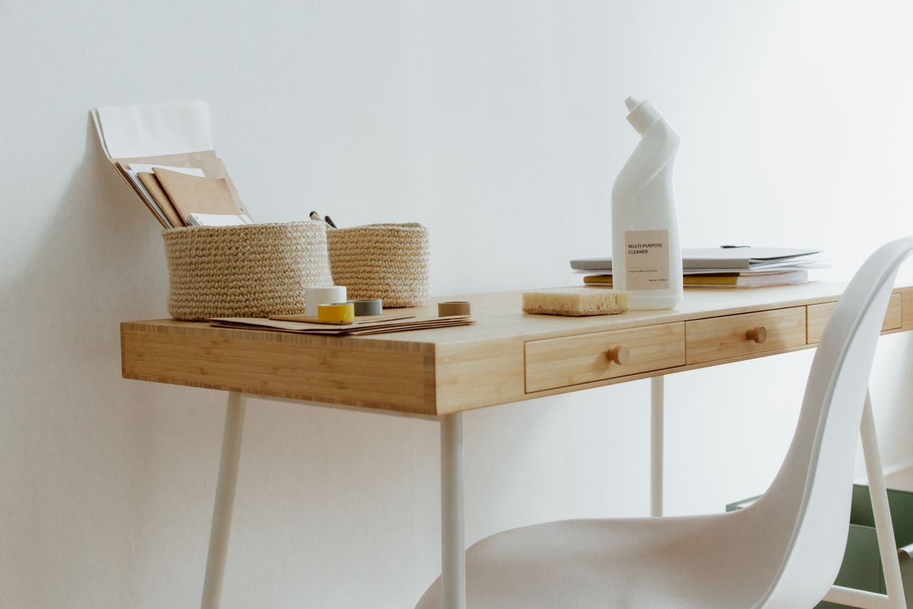 who-we-are A clean and organized home office desk with cleaning products, papers, and storage baskets.